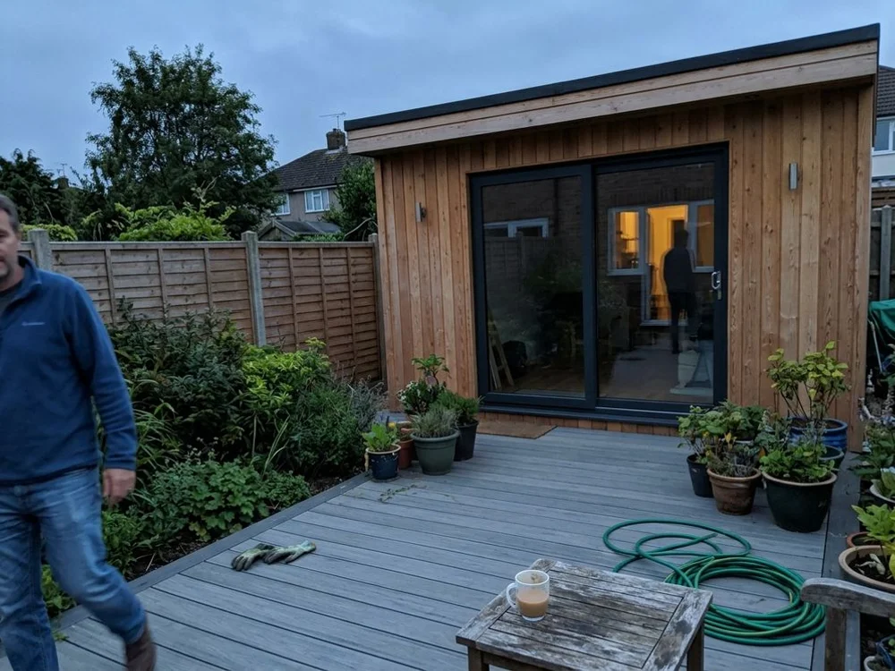 Larch-clad garden room with aluminium sliding doors in Dunstable at dusk