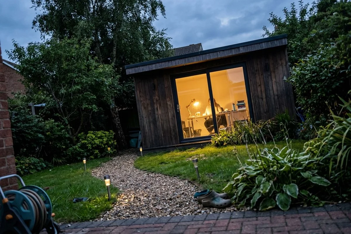 Wide shot of a bespoke garden office at dusk with warm interior lighting